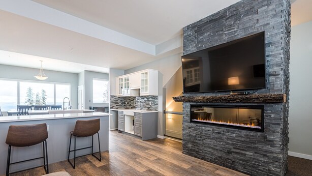 A modern kitchen with a stone accent wall, a flat-screen TV, and a built-in fireplace.
