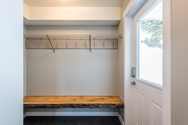 A small, enclosed closet with a wooden bench, a metal coat rack, and a door with a window.