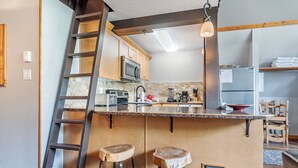 A kitchen with a central island, wooden stools, a ladder, and a microwave. - Cozy Ski-In/Out Retreat with Hot Tub & BBQ (Vernon)