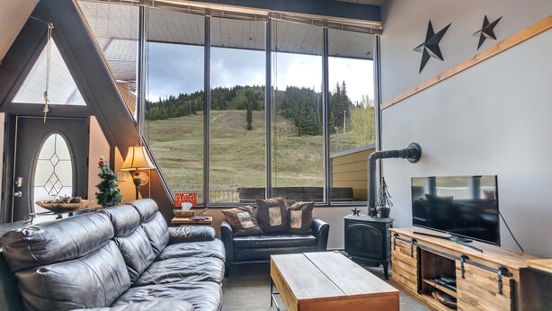 A modern living room with a leather sofa, a wooden coffee table, a TV, and a fireplace. - Cozy Ski-In/Out Retreat with Hot Tub & BBQ (Vernon)