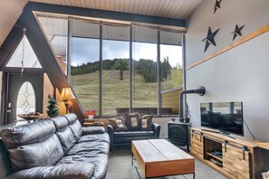 A modern living room with a leather sofa, a wooden coffee table, a TV, and a fireplace. - Cozy Ski-In/Out Retreat with Hot Tub & BBQ (Vernon)