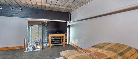A room with a bed, a television on a stand, a window, and a door leading outside.