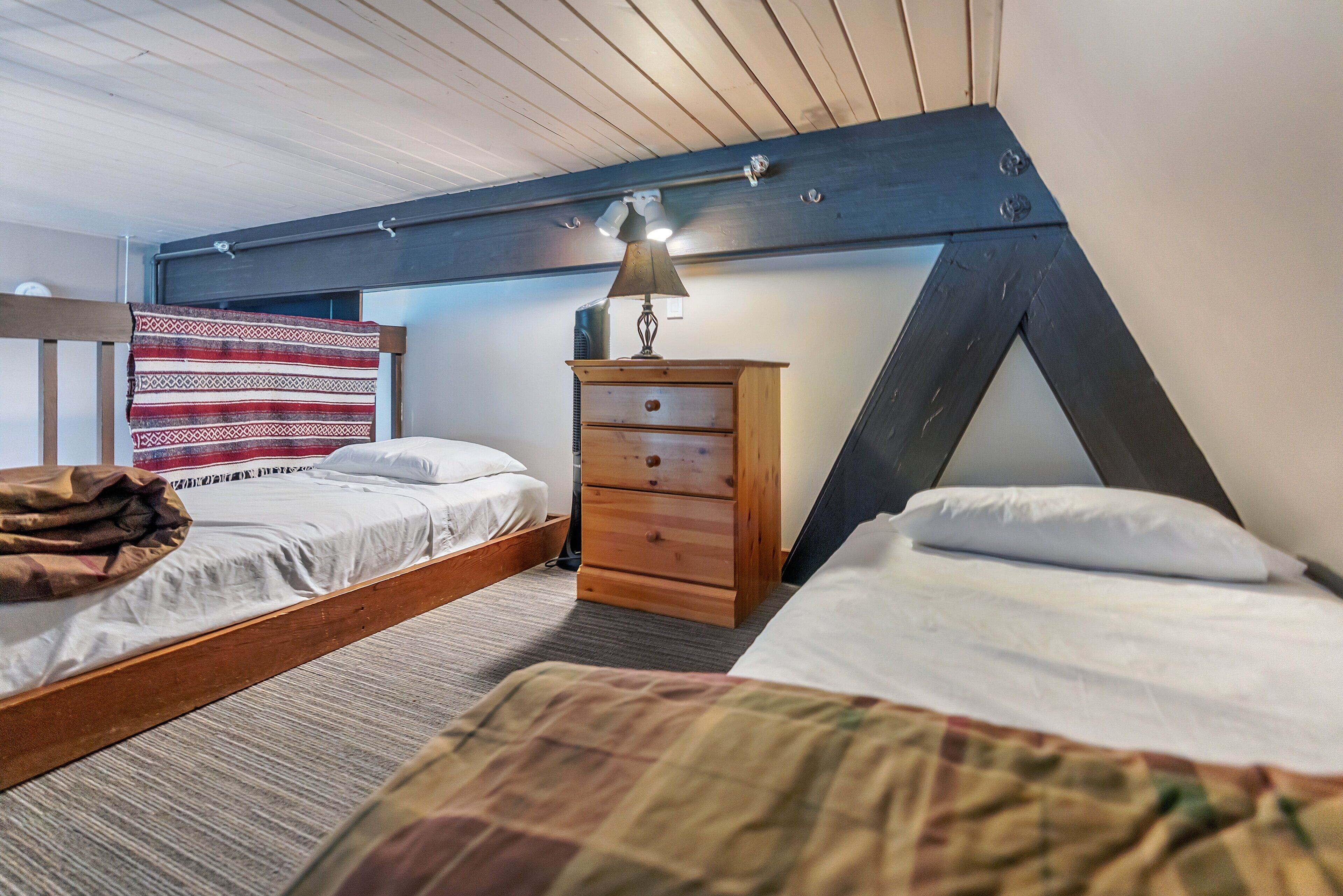 Une chambre avec deux lits, une commode en bois, une lampe et une couverture à motifs.