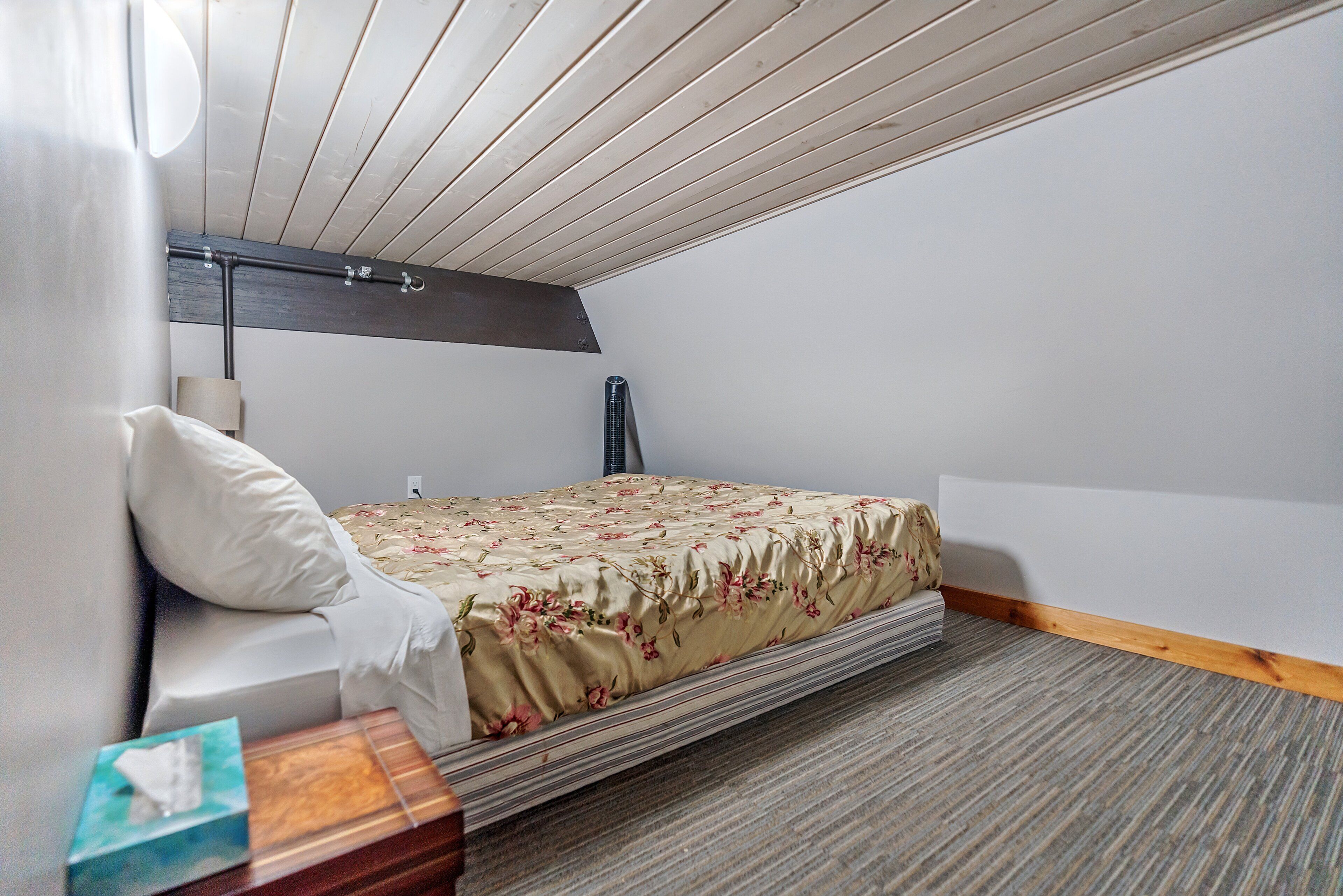 Ein Schlafzimmer mit Bett, Nachttisch, Lampe und Holzbalkendecke.