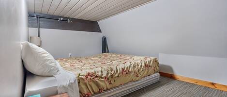 A bedroom with a bed, a nightstand, a lamp, and a ceiling with wooden beams.