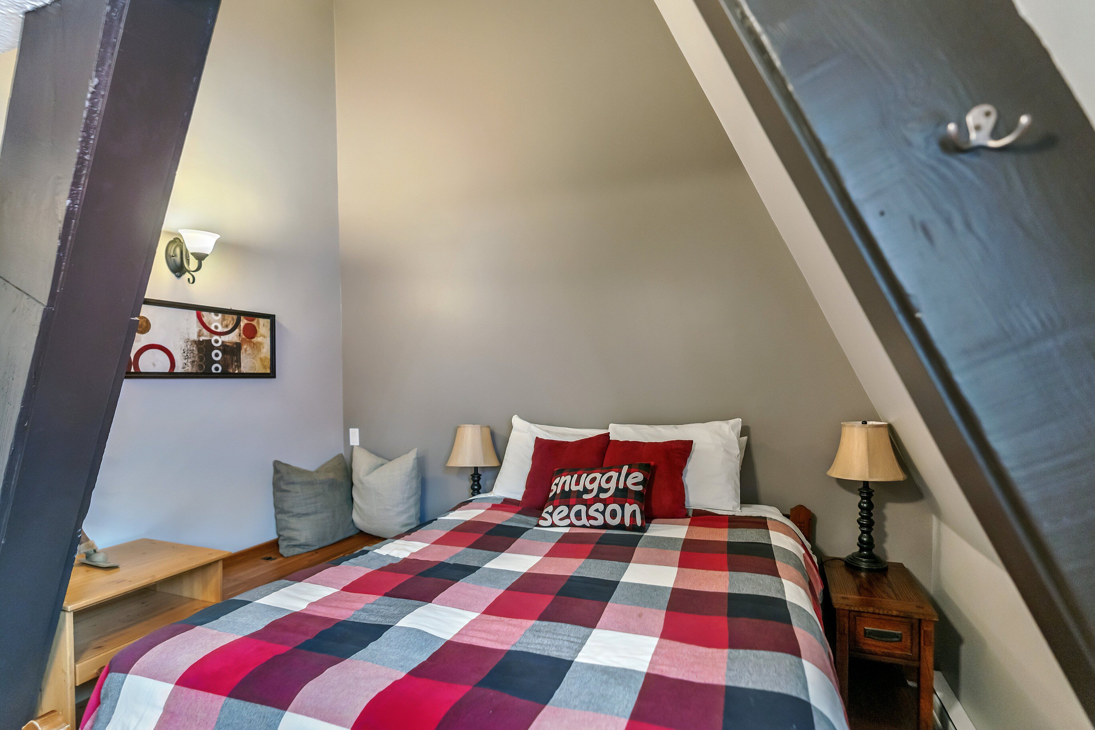 A bedroom with a checkered bedspread, a bedside table with a lamp, and a wall-mounted light fixture.