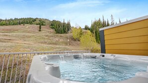 A hot tub on a balcony with a view of a grassy field and trees. - Cozy Ski-In/Out Retreat with Hot Tub & BBQ (Vernon)