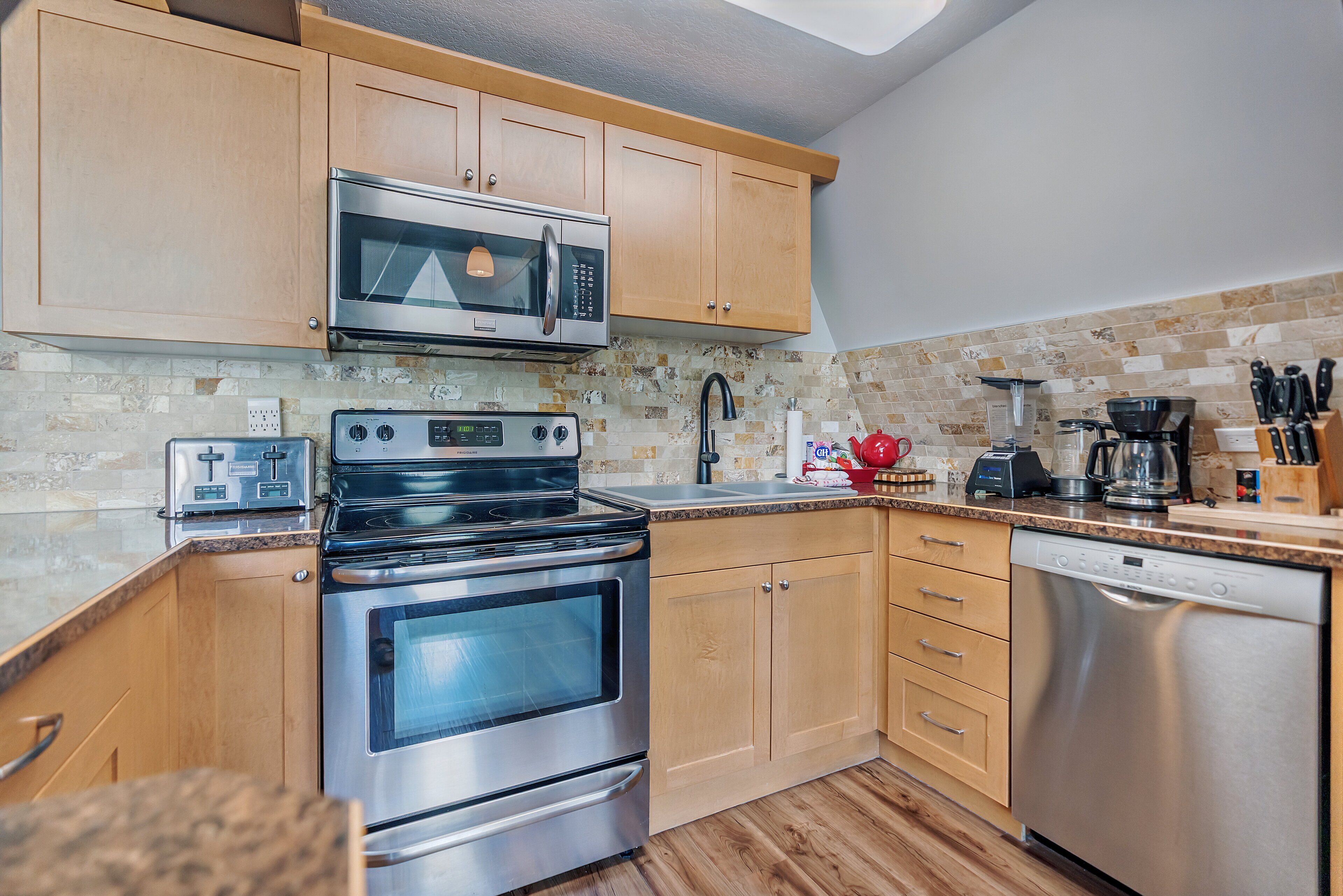 A modern kitchen with wooden cabinets, stainless steel appliances, a toaster, and a dishwasher.