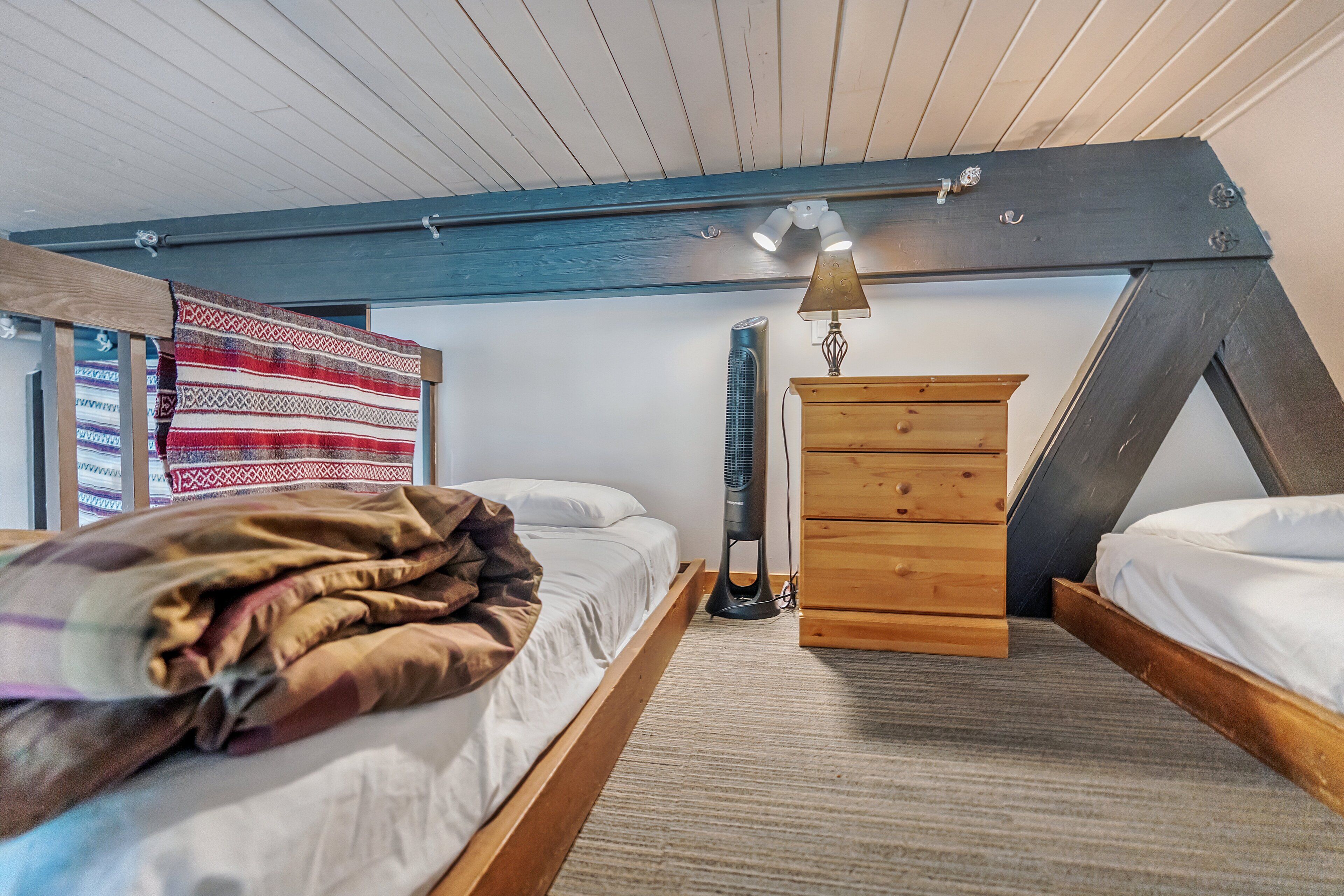 Ein Schlafzimmer mit zwei Betten, einer Holzkommode, einem Standventilator und einer gemusterten Decke.