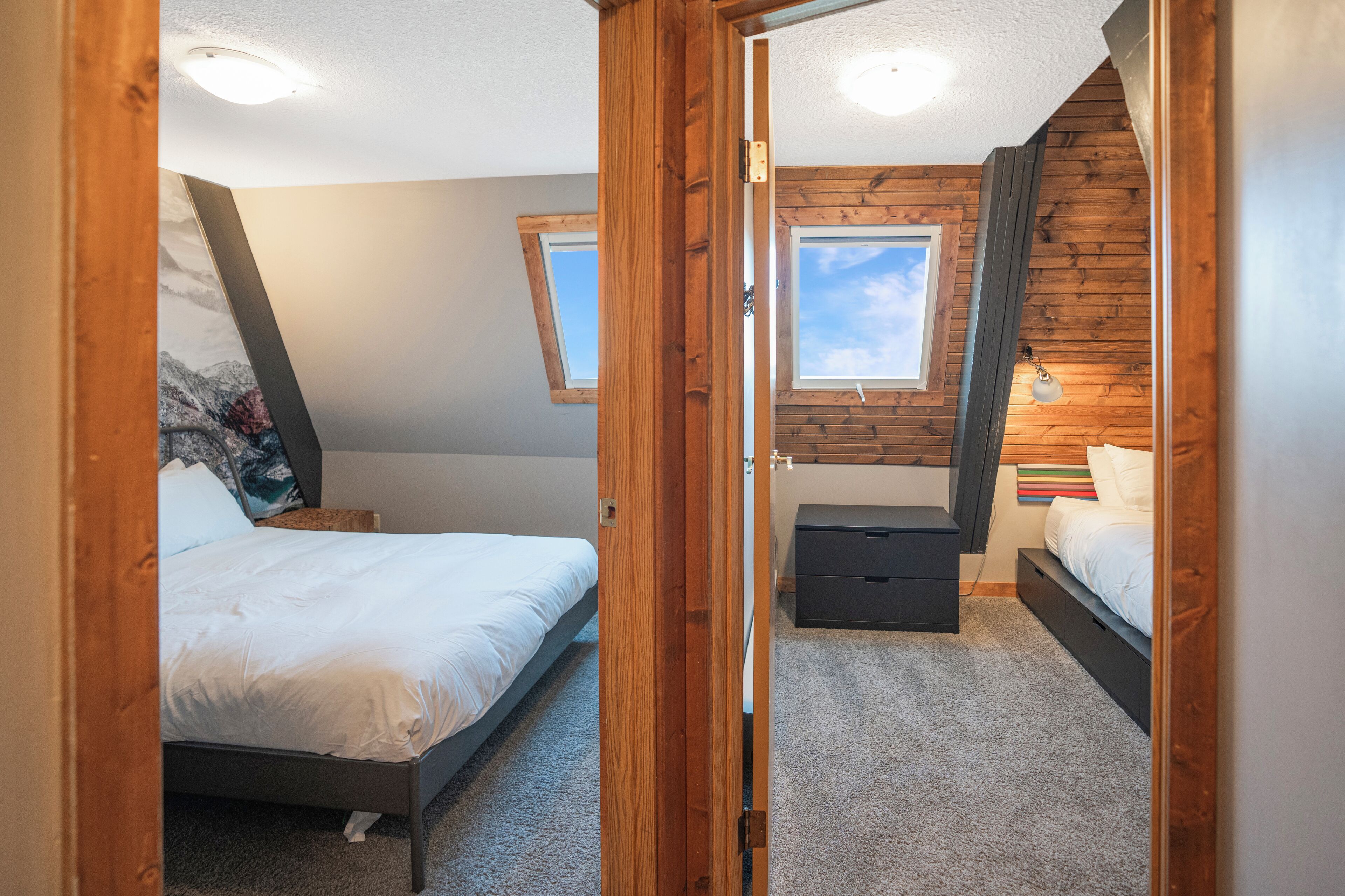 A bedroom with a sloped ceiling, a bed, a dresser, and a window.