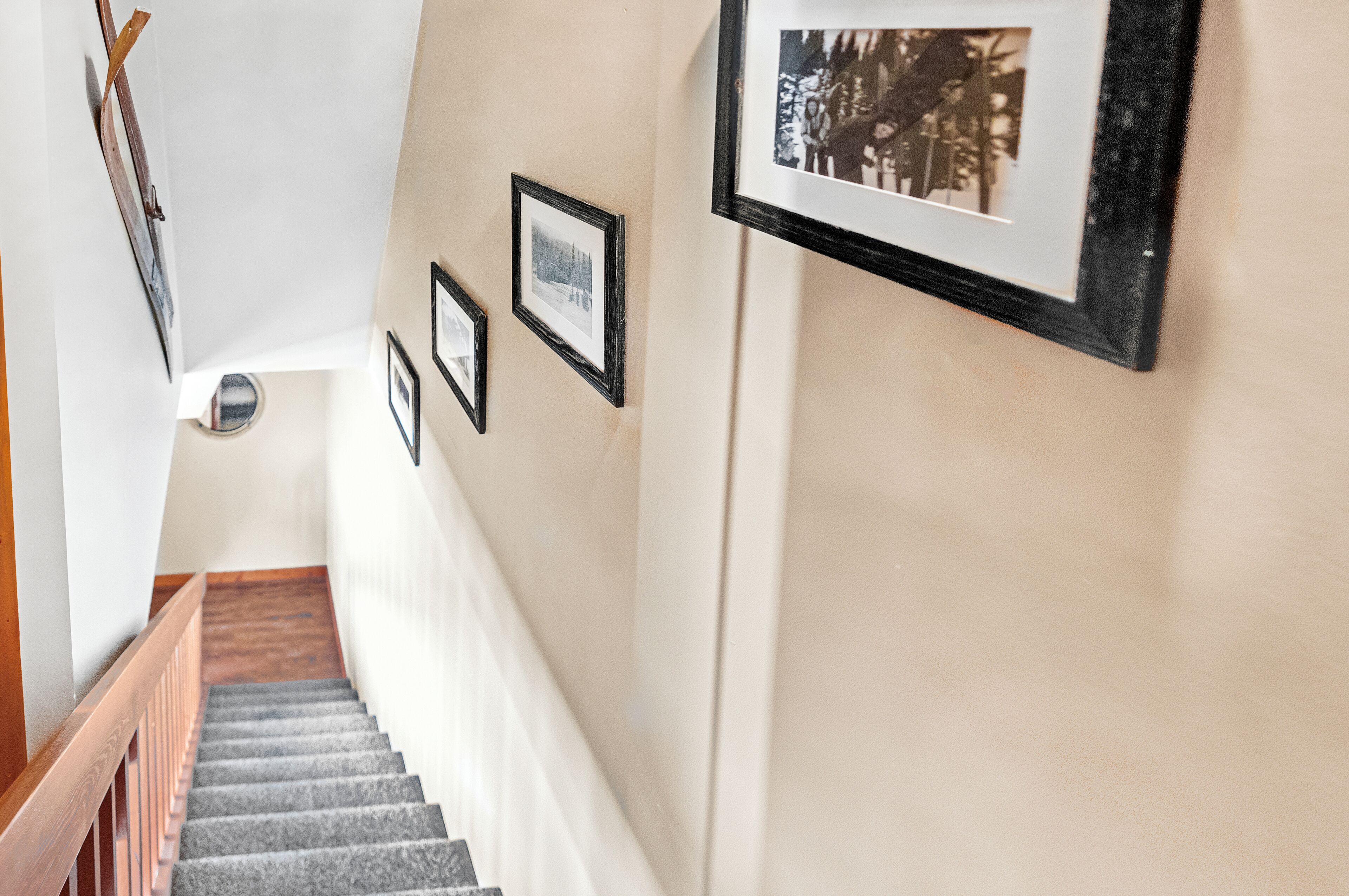 Eine Treppe mit hölzernem Geländer, die zu einer Zwischenebene führt, an deren Wand Bilder in Rahmen hängen.