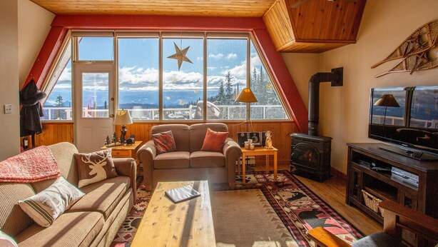A cozy living room with a large window, a wooden ceiling, a television, and a fireplace.