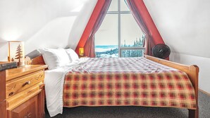 A bedroom with a bed, a wooden dresser, a nightstand, a window with a view of trees, and a red curtain.