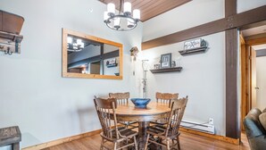 A dining area with a round wooden table, six wooden chairs, a chandelier, a mirror, and a clock on the wall. - Charming 2-Bedroom Suite – Perfect for Families & Groups (Vernon)