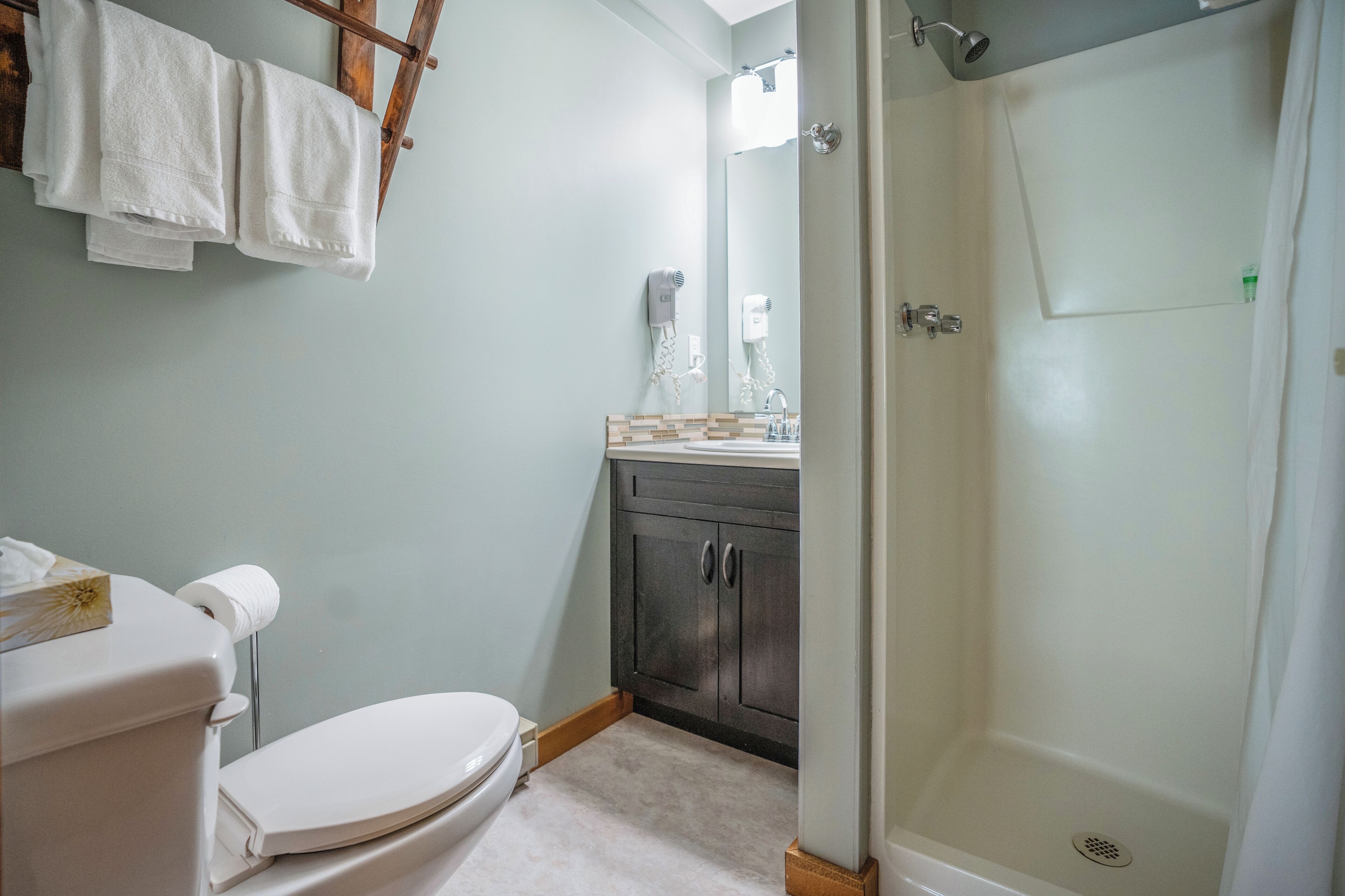 A bathroom with a toilet, a sink, a shower, and towels hanging on a rack.