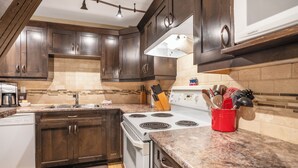 A modern kitchen with dark wooden cabinets, a white stove, and granite countertops. - Charming 2-Bedroom Suite – Perfect for Families & Groups (Vernon)