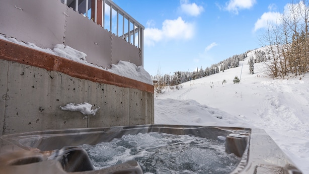 Un jacuzzi con vistas a un paisaje nevado y un edificio con balcón.