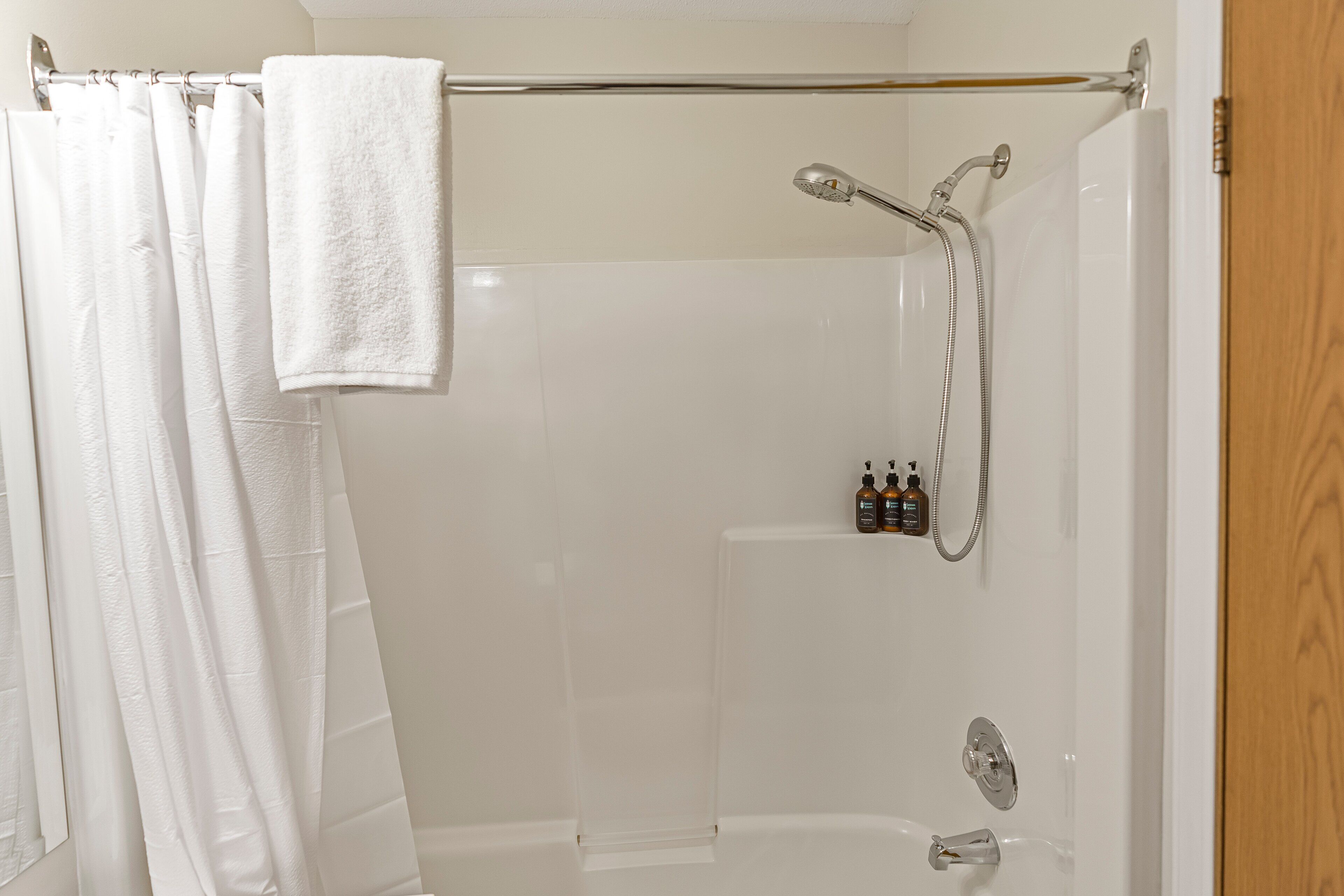 Un espace douche doté d’une porte en verre, une serviette suspendue à une tringle et deux bouteilles de shampoing et d’après-shampoing fixées au mur.
