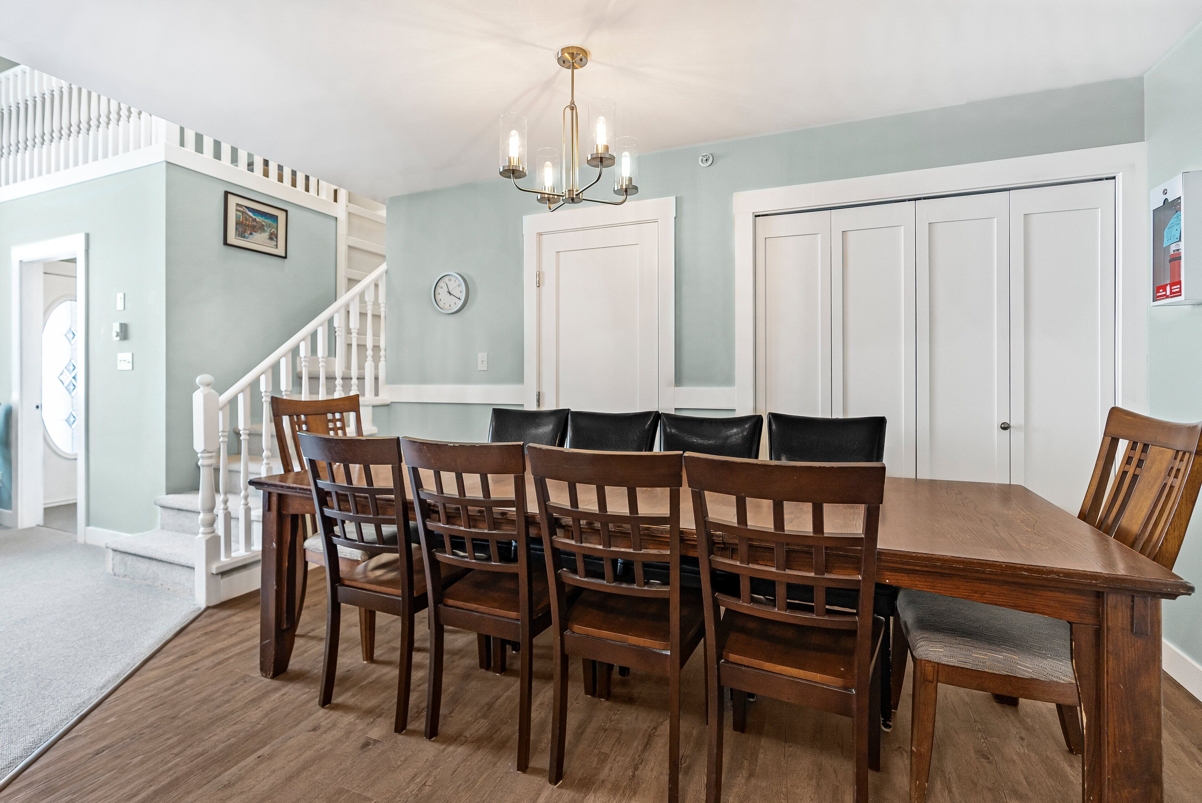 A dining area with a wooden table and chairs, a chandelier, and a staircase leading to another room.