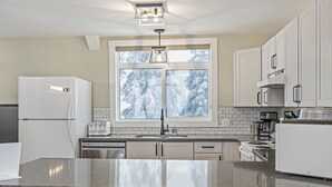 A modern kitchen with a large window, white cabinets, a built-in oven, and a stainless steel refrigerator.