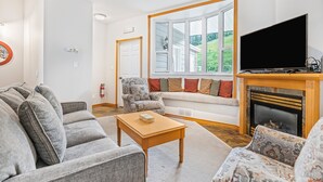 A living room with grey sofas, a wooden coffee table, a fireplace, and a large window with a view of greenery. - Bright & Spacious Property w/ Fireplace & Hot Tub - Sleeps 13 (Vernon)