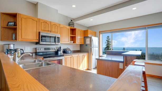 A modern kitchen with wooden cabinets, stainless steel appliances, and a large window offering a view of the ocean. - Bright & Spacious Property w/ Fireplace & Hot Tub - Sleeps 13 (Vernon)