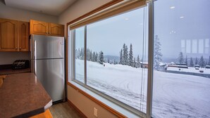 A kitchen with wooden cabinets, a stainless steel refrigerator, and a large window offering a view of a snowy landscape. - Bright & Spacious Property w/ Fireplace & Hot Tub - Sleeps 13 (Vernon)