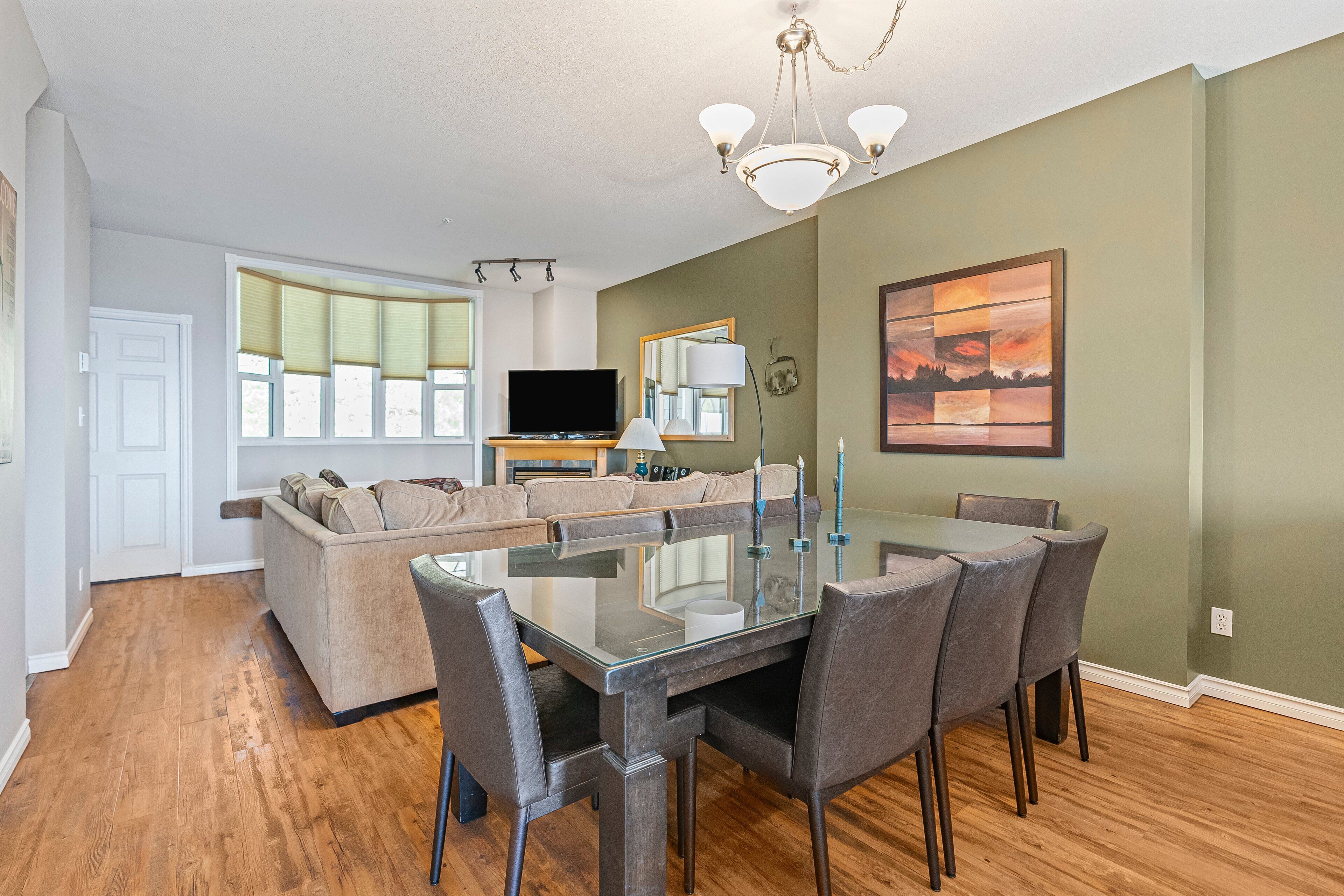 A modern living room with a glass-top dining table, grey chairs, a beige sofa, and a flat-screen TV.