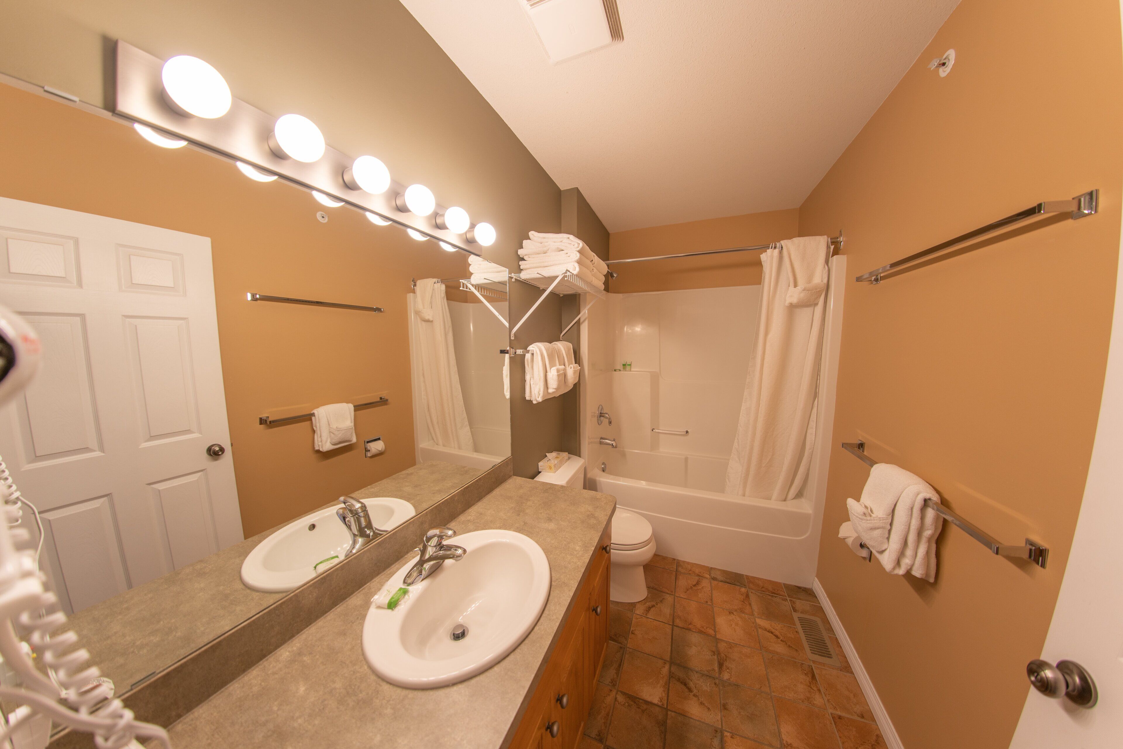 A bathroom with two sinks, a mirror with lights, a bathtub, and a shower curtain.