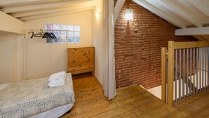 A room with a wooden bed, a wooden dresser, a brick wall, and a window with multiple panes.