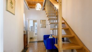 A hallway with a wooden staircase, a blue sofa, and a kitchen area in the background.