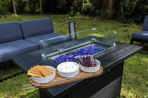 Une table à plateau en verre, sur laquelle sont disposés des en-cas et des chamallows, installée à l’extérieur, avec un canapé en arrière-plan.