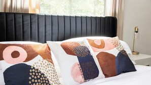 A bed with a black upholstered headboard and decorative pillows with geometric patterns. - 4BR Charm, 5 min to UF, Firetable, Big backyard, King Bed, Games, BBQ, Joy (Gainesville)
