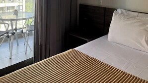 Une chambre d’hôtel avec un lit, une petite table et une vue sur un immeuble par la fenêtre.