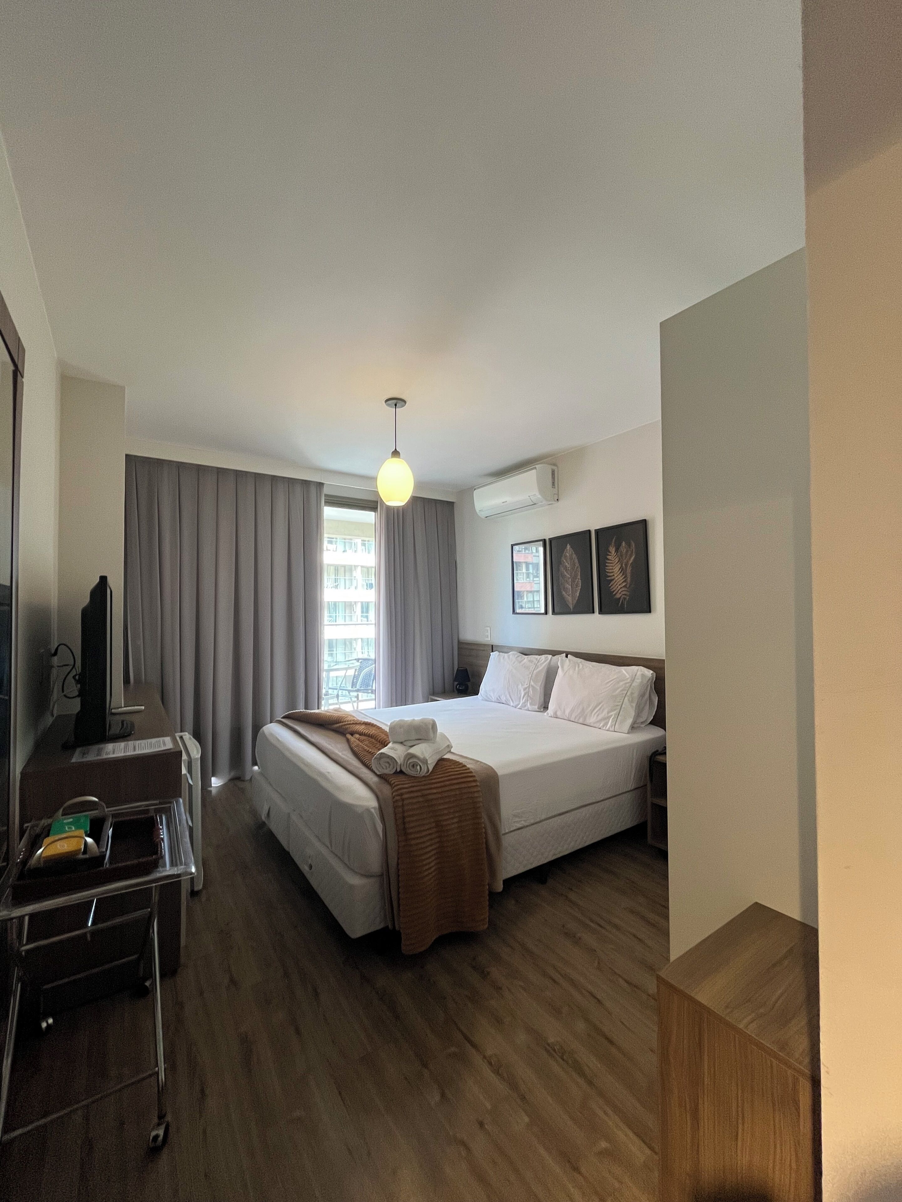 Ein Hotelzimmer mit Bett, Nachttisch, Lampe und Blick nach draußen.