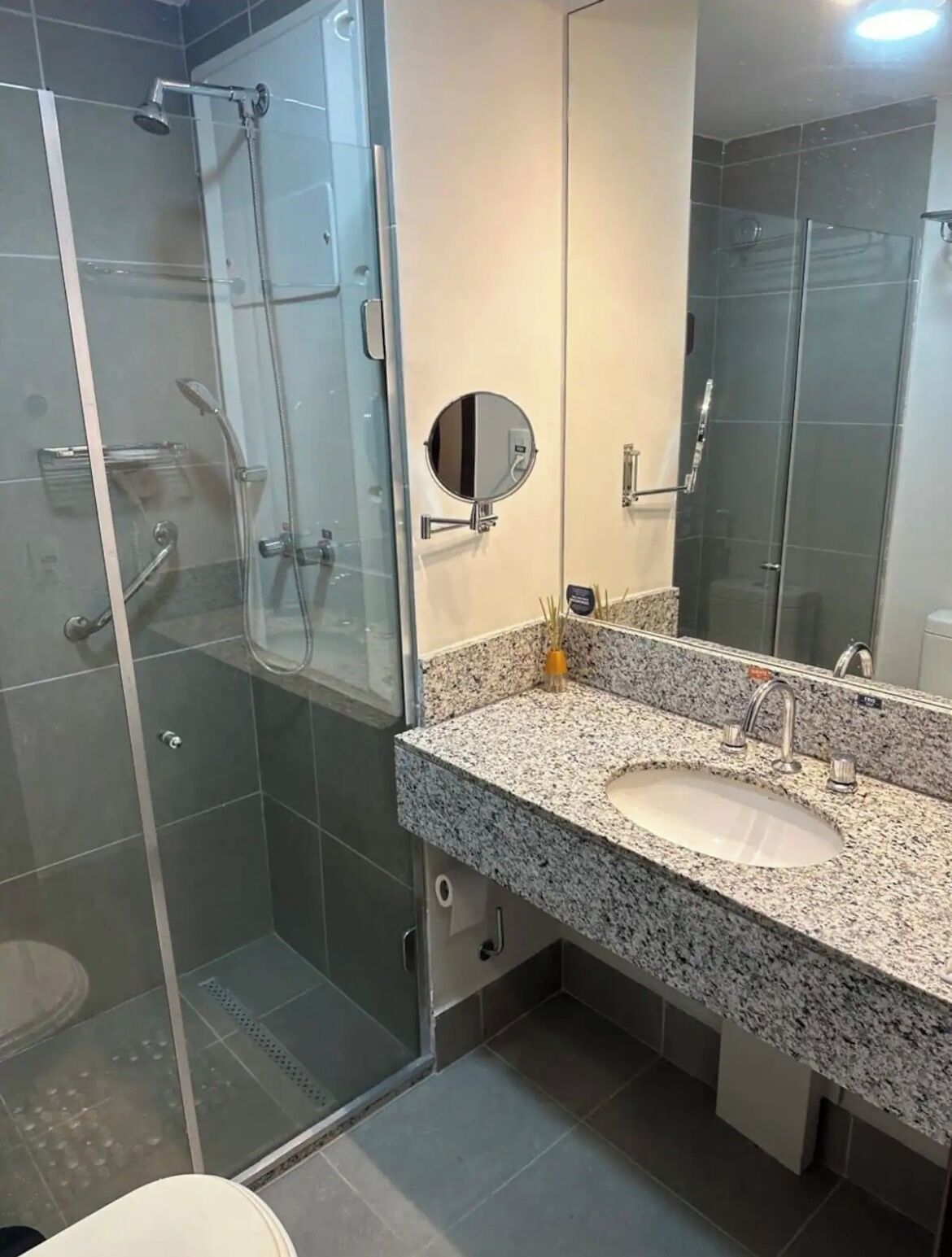 A modern bathroom with a glass-enclosed shower, a granite countertop sink, and a large mirror.