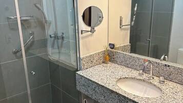 A modern bathroom with a glass-enclosed shower, a granite countertop sink, and a large mirror.