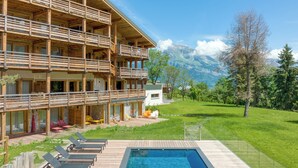 Un immeuble en bois à plusieurs étages, doté de balcons, d’une piscine et offrant une vue sur les montagnes.