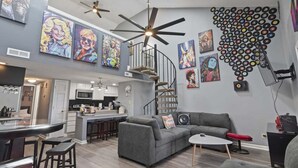 A modern interior with a grey sofa, a white coffee table, a kitchen area, and a spiral staircase. - Rhythm Retreat  | Bar, Patio & Space for 10 (Myrtle Beach)
