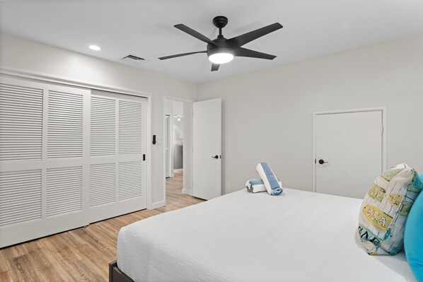 Une chambre à coucher comprenant un lit, un ventilateur de plafond, une armoire et une porte donnant sur une autre pièce.