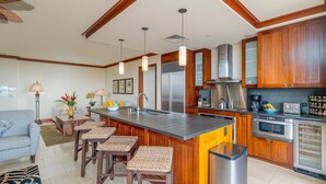 Une cuisine moderne avec des meubles en bois, un réfrigérateur en acier inoxydable, un four encastré et un coin bar avec des tabourets.