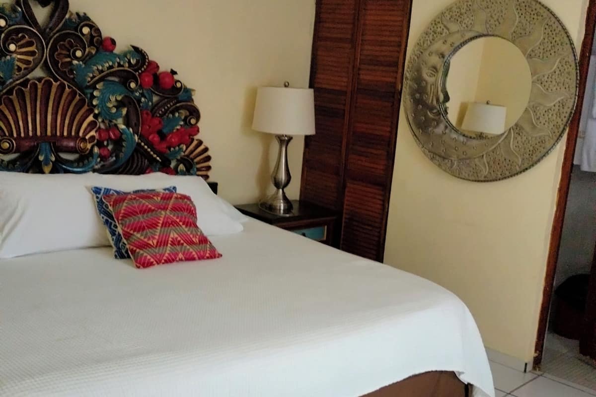 A neatly made bed with a brown bed skirt, a decorative headboard, and a red pillow.