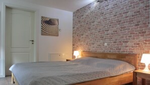 A bedroom with a wooden bed, a brick wall, and a door. - Only approx. 300 m to the fine sandy beach close to Warnemünde in Markgrafenheide. - (Rostock)