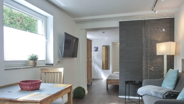 A modern, well-lit room with a wooden dining table, a grey sofa, and a TV mounted on the wall. - Only approx. 300 m to the fine sandy beach close to Warnemünde in Markgrafenheide. - (Rostock)
