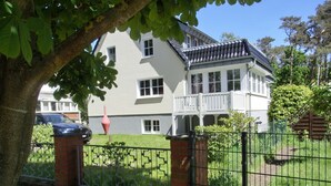 A two-story house with a white exterior, a balcony, and a brick gate. - Only approx. 300 m to the fine sandy beach close to Warnemünde in Markgrafenheide. - (Rostock)