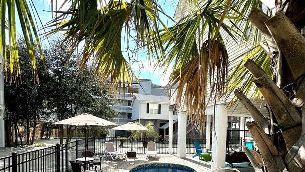 An outdoor swimming pool area with lounge chairs and umbrellas, surrounded by palm trees and a brick walkway. - 3-bedroom, 2.5-bathroom, sleeps 10 people with heated pool and elevator. (Murrells Inlet)