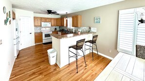 A spacious kitchen with wooden cabinets, a central island with bar stools, a ceiling fan, and a view of the beach through the window. - 3-bedroom, 2.5-bathroom, sleeps 10 people with heated pool and elevator. (Murrells Inlet)