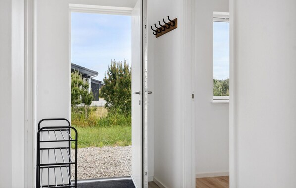A white door with a metal gate, a coat hook, and a view of a house and greenery outside.