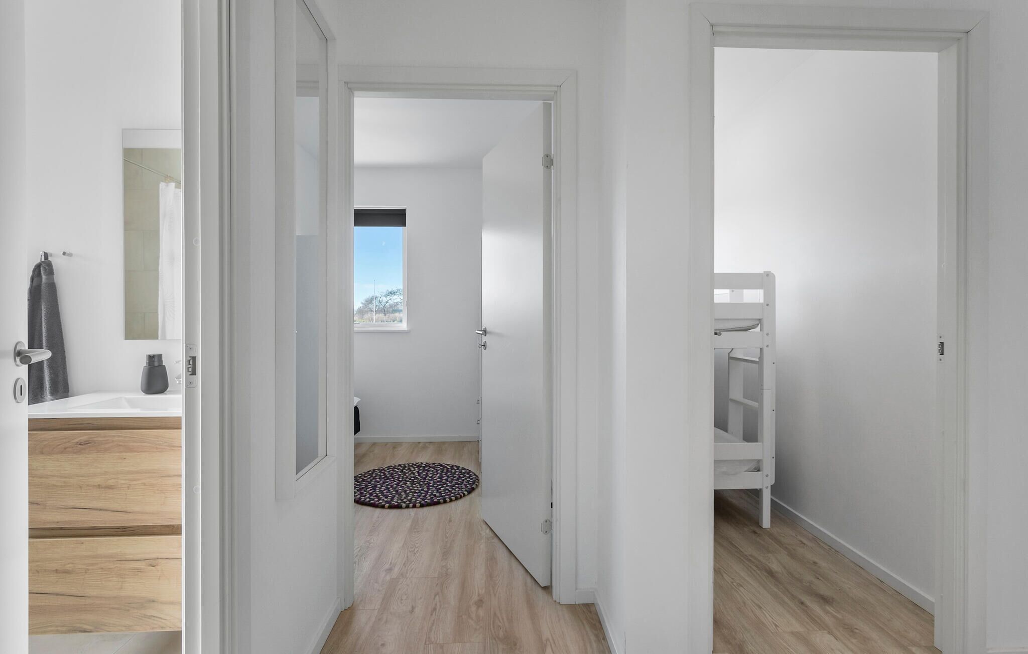 Un couloir avec un plancher en bois, une porte blanche et une petite fenêtre.