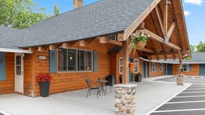 A log cabin-style building with a covered patio area, outdoor seating, and a stone planter.